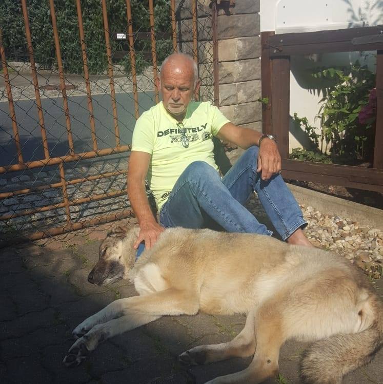 Rüdiger Squarra sitzt auf dem Boden und streichelt einen Hund, der neben ihm liegt.